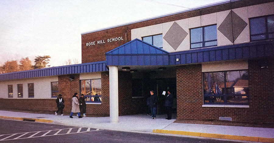 Color photograph of Rose Hill Elementary School taken in 1994. The large banks of windows have been removed and have been replaced by smaller energy-efficient windows. The exterior brick-work has been updated and covered over in places with a new facade. The first story awning is painted a bright blue.  