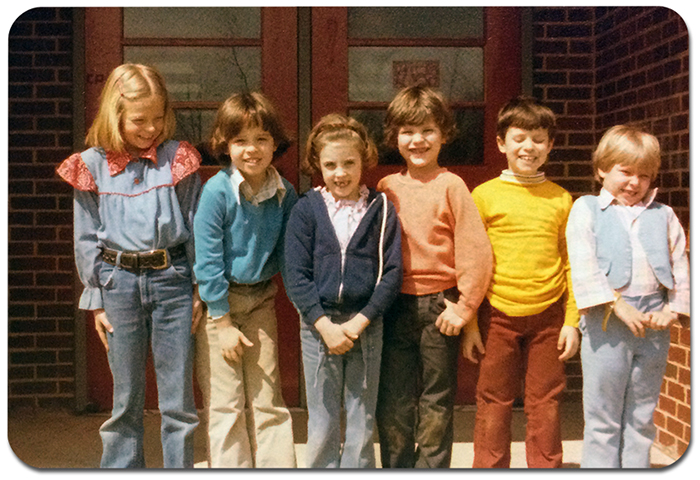 Color photograph, taken around 1980, showing six children standing in front of the main entrance to Rose Hill Elementary School. The children are smiling and giggling.  